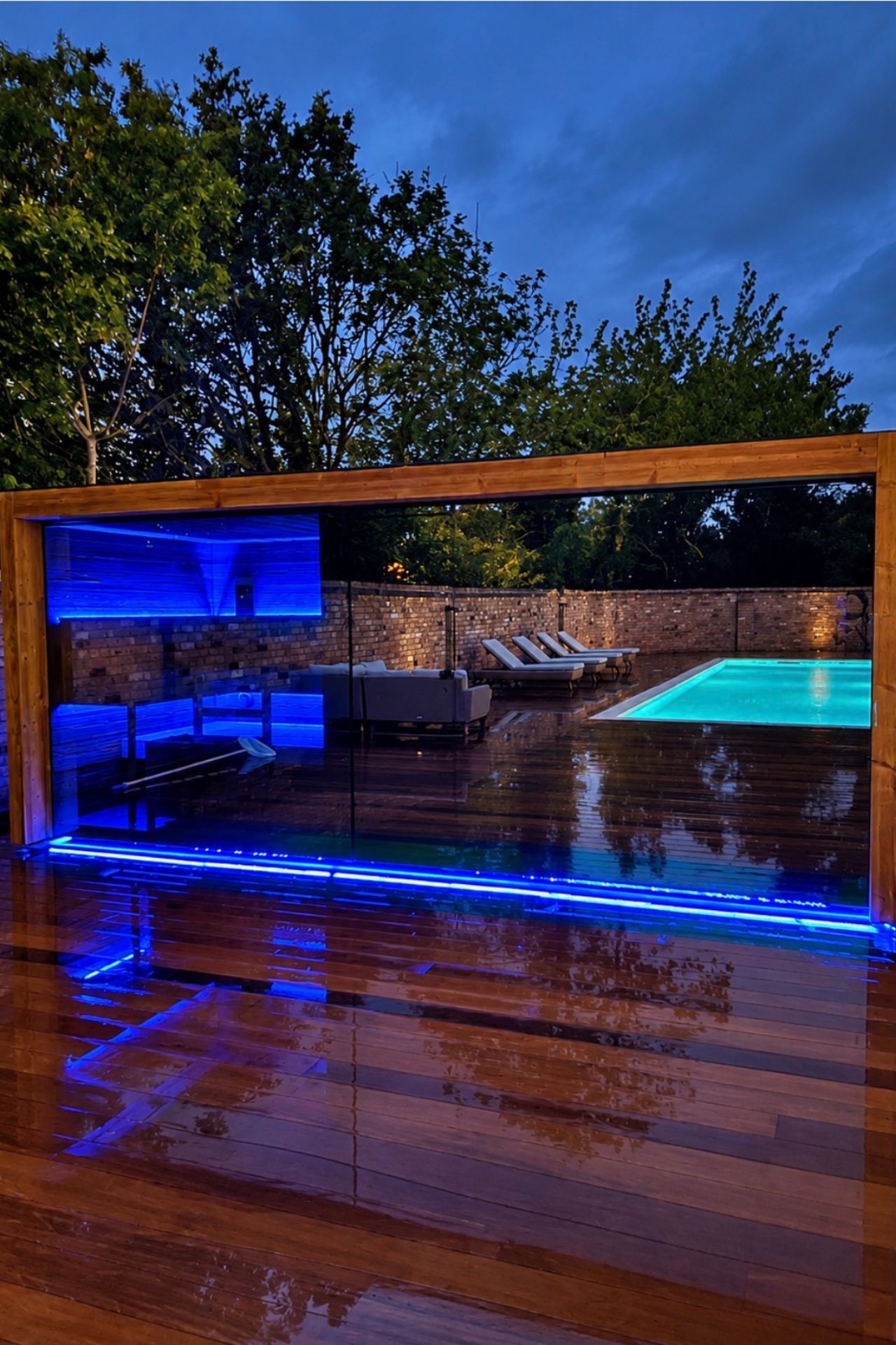 Mirrored-glass NN sauna lit at dusk, reflecting the swimming pool